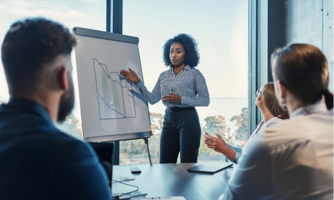 Project Manager Officer Jeune femme en chemise blanche fait une présentation face à plusieurs personnes dans une salle de réunion