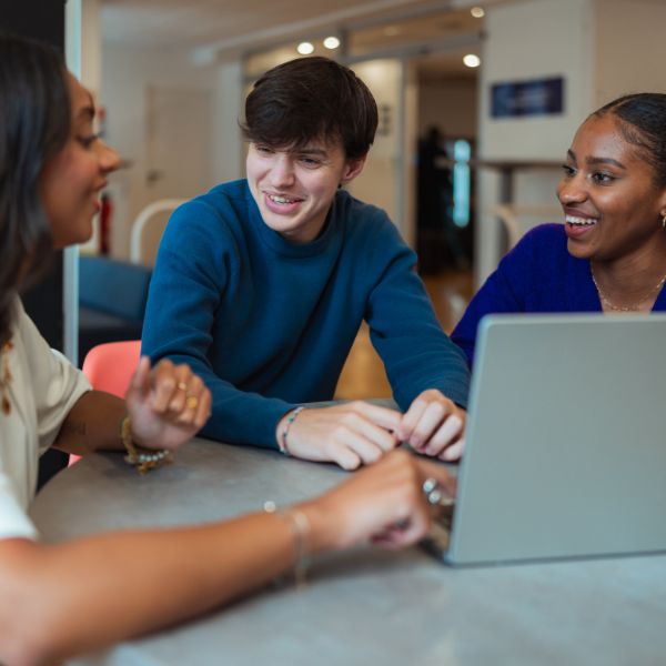 Etudiants en Bachelor : Marketing d'influence et Brand Content Trois étudiants assis autour d'une table avec un ordinateur dessus et discutent