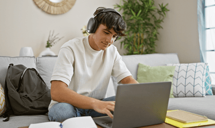 Jeune homme avec un t-shirt blanc et un casque audio travaille sur un ordinateur portable dans son salon