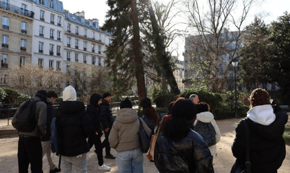 Etudiants de dos dans un parc avec un professeur et en arrière plan des immeubles parisiens et des sapins
